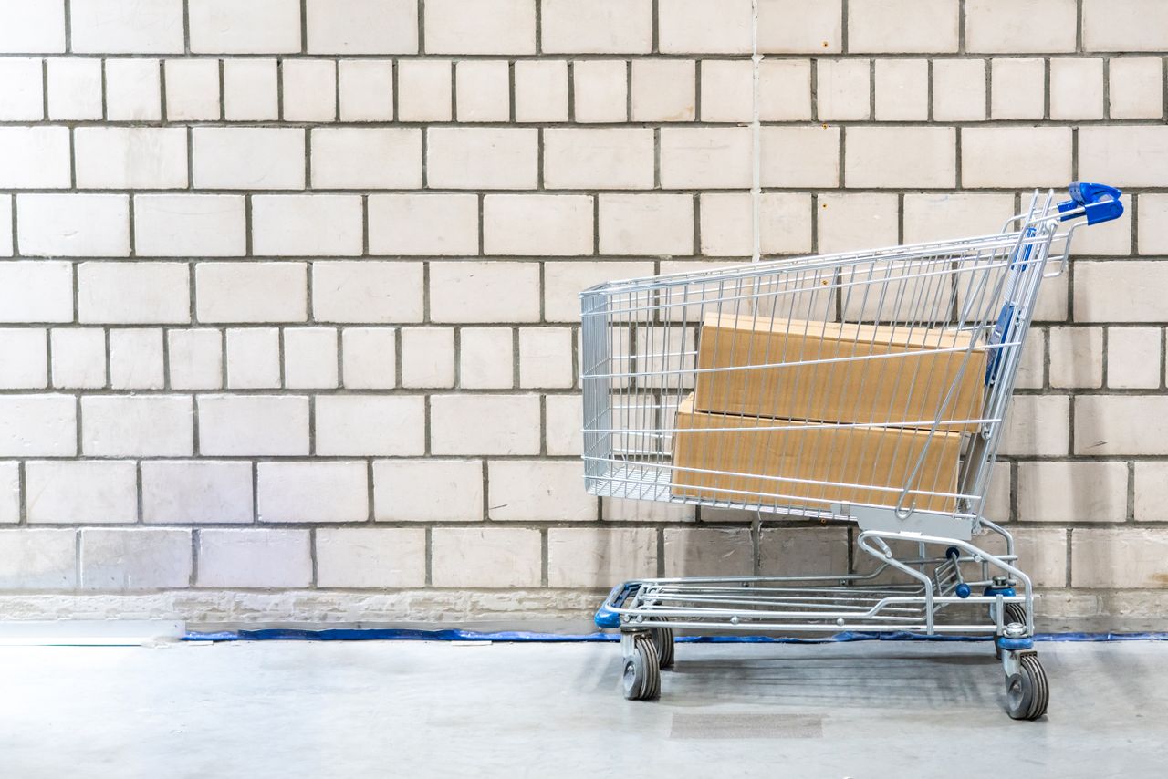 Shopping cart with cardboard boxes against a concrete block wall. Minimalist and industrial setting.